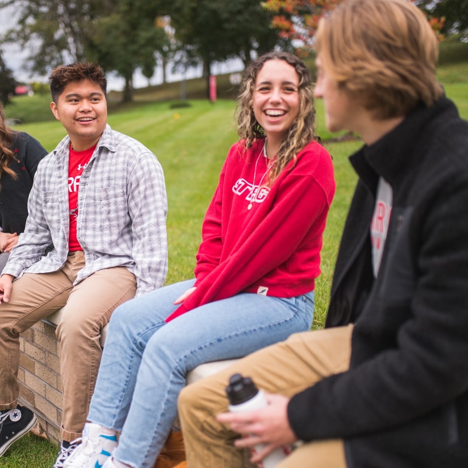 A group of four students sit together on a stone wall at ýƵƹۿ, sharing smiles and good times.  